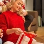 Woman in red sweater and Santa Hat opening a gife