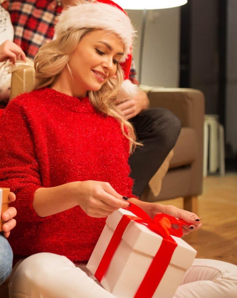 Woman in red sweater and Santa Hat opening a gife