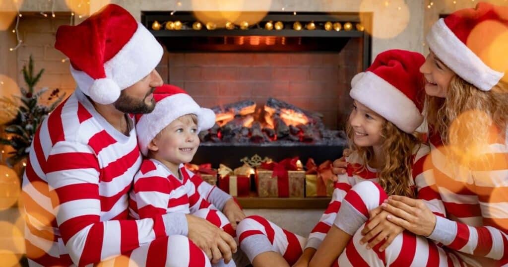 family sitting around fireplace in matching christmas pajamas