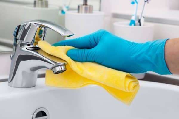 gloved hand cleaning a dirty sink faucet