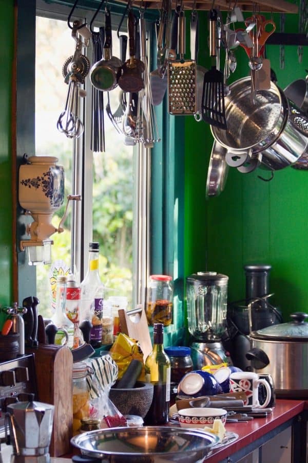 cluttered kitchen with lots of pots, pans, dishes, and small appliances on the counters