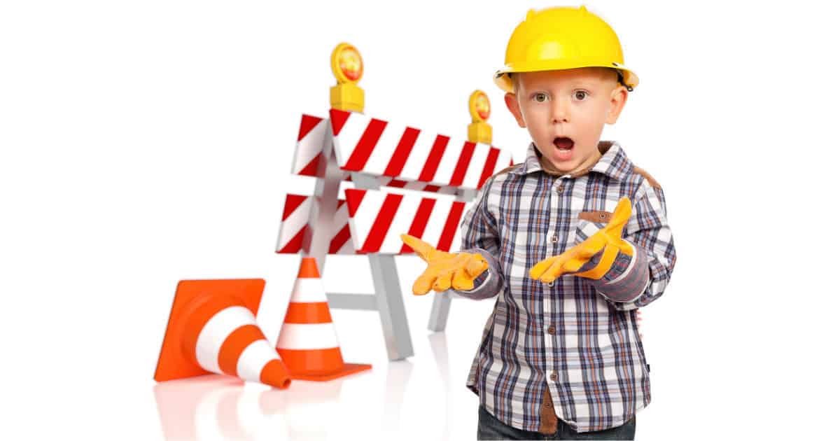 shocked young boy in construction hat standing in front of roadblock 