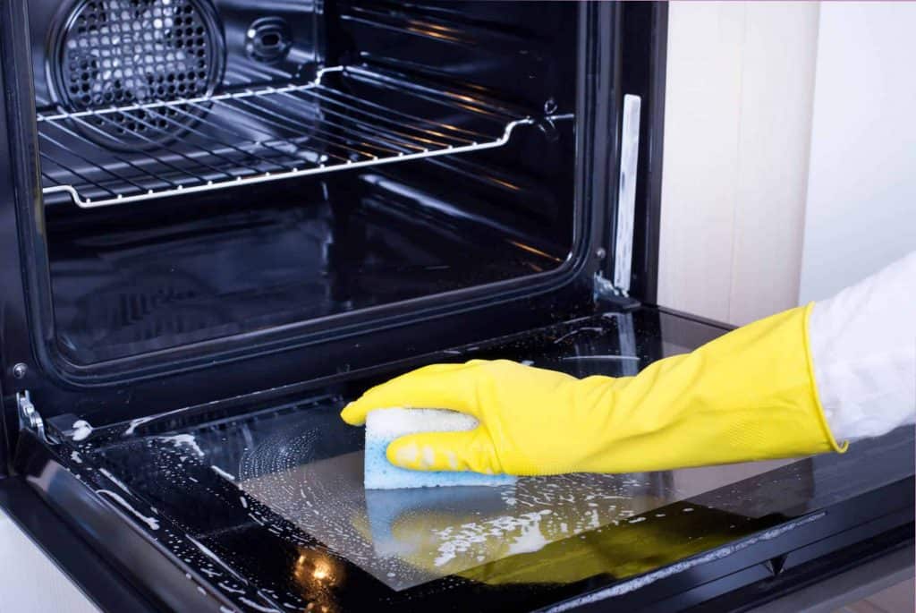 Gloved hand with sponge deep cleaning the oven.