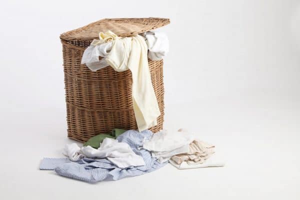 Full laundry hamper with dirty clothes on the floor next to it