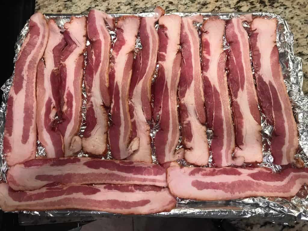 bacon slices laid out on a foil covered jelly roll pan for baking