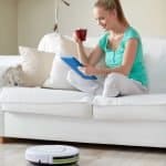 lady sitting on the couch with a cup of coffee while a robot vacuum cleans the floors