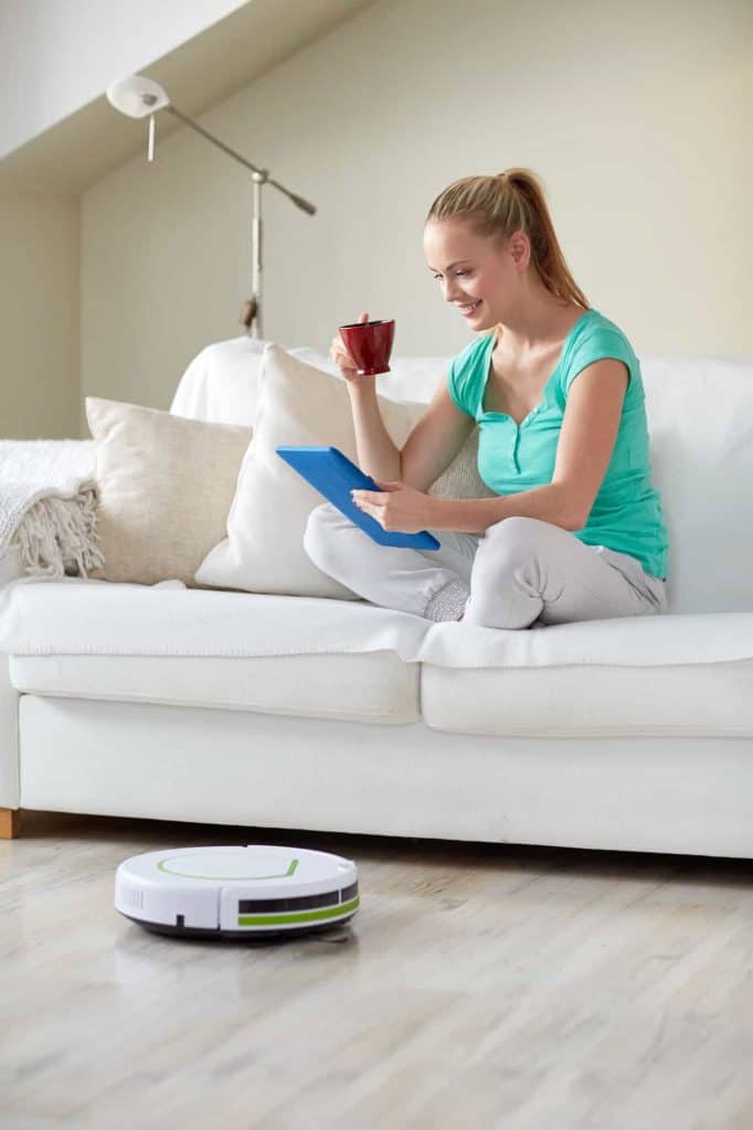 lady sitting on the couch with a cup of coffee while a robot vacuum cleans the floors