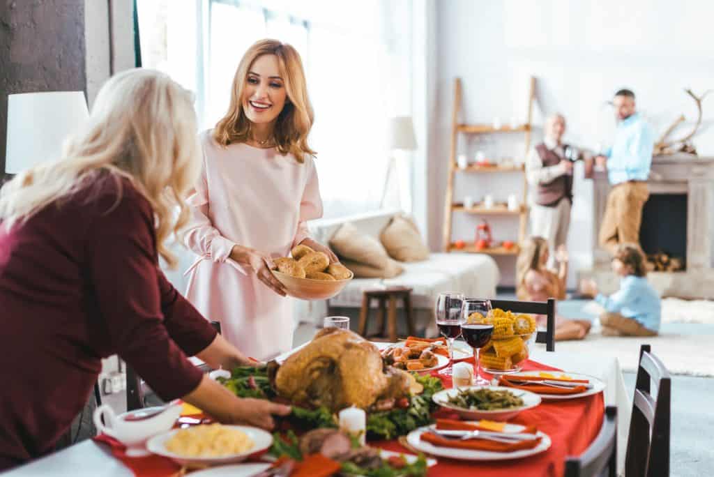 Women serving a stress-free Thanksgiving meal with family socializing in the background