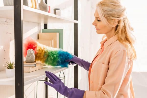 Woman dusting bookshelf while speed cleaning to get ready for company