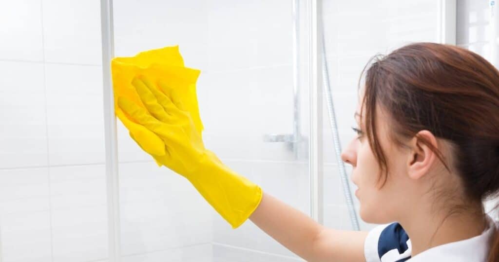 woman cleaning hard water stains off of glass shower doors