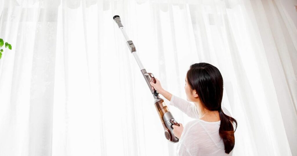 woman vacuuming dusty curtains